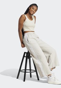 Φωτεινός μπεζ κοντός τοπ και παντελόνι με φαρδιά πόδια με λευκές ρίγες στο πλάι, καθισμένο σε μια μαύρη σφαίρα, σε συνδυασμό με λευκά αθλητικά.