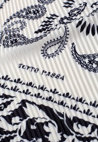 Tissu blanc plissé avec motifs paisley et floraux noirs, avec le texte "TUTTO PASSA" en noir.