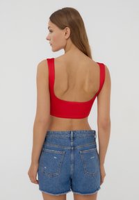 Top rosso corto con spalline larghe e schiena bassa, abbinato a pantaloni shorts in denim blu con orli sfrangiati e tasche posteriori.