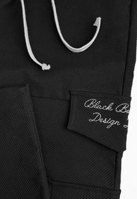 Zwarte stof met een textuurpatroon, met witte trekkoorden en een genaaid label met de tekst "Black Ball Design."