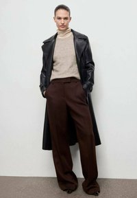 Cappotto di pelle nera sopra un dolcevita lavorato a maglia beige, abbinato a pantaloni marroni larghi. Texture morbide e colori neutri dominano l'outfit.