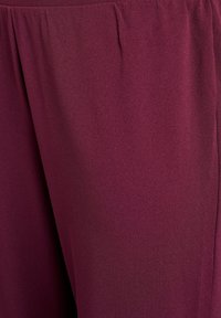 Burgunďský materiál s hladkým povrchem, s jemnými sklady v oblasti pasu pro uvolněný střih. Bez viditelných vzorů nebo kovových prvků.