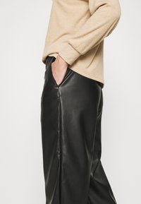 Svarta läderbyxor med en slät textur, sidoficka och rak ben-design, tillsammans med en ljusbeige ribbad tröja.