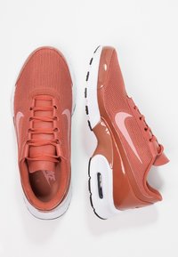 Nike sneakers in coral mesh with glossy accents, white midsole, black outsole, and subtle pink swoosh. Laced design, padded collar.