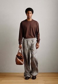 Chemise marron à manches longues, pantalon ample à motifs, sac en cuir marron et chaussures foncées ; caractéristiques d'un fit décontracté et d'un tissu texturé.