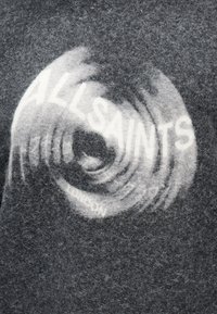 Tissu gris foncé et duveteux avec un motif en spirale blanche et un texte partiellement visible indiquant "ALLSAINTS" en lettres majuscules.