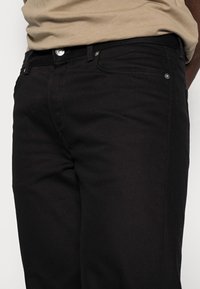 Black denim jeans with a slim fit, featuring a traditional button and zipper closure, and front pockets. The fabric has a matte finish.