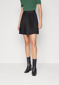 Gonna plissettata nera con vita piatta, abbinata a stivali neri alla caviglia. Il tessuto ha una texture liscia e un design strutturato.