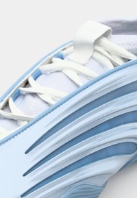 Lyseblå sportssko med en tekstureret overdel, fleksible overlays, hvide snørebånd og et glansfuldt buet design med lagdelte detaljer.
