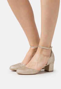 Glittering gold block-heeled shoes with an ankle strap and rounded toe. Sparkling texture and smooth surface, providing a secure fit.