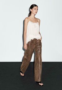Light, flowing white camisole with ruffled hem paired with brown leather wide-leg pants. Plain design, soft texture, minimal hardware.