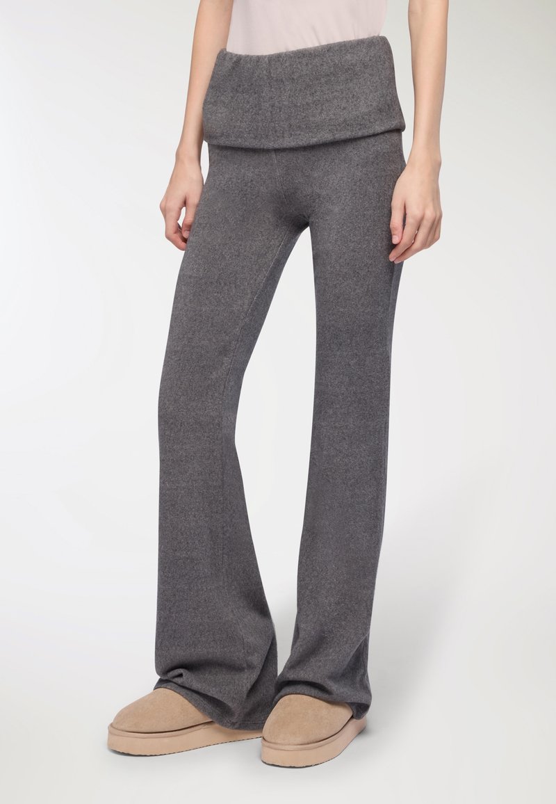 Szare, rozszerzane spodnie dzianinowe z szerokim, złożonym paskiem w talii. Miękka tekstura, noszone z beżowymi kapciami.