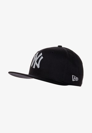 Gorra de béisbol negra con un logotipo de los New York Yankees bordado en plata en alto relieve en la parte frontal, con visera plana y agujeros de ventilación.