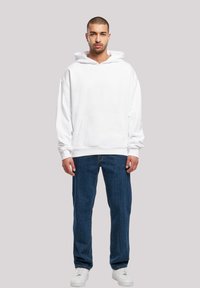 White hoodie with a front pocket and drawstring hood, paired with blue denim jeans and white sneakers. Simple and loose-fitting design.