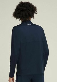 Giacca atletica a maniche lunghe blu navy realizzata in tessuto elastico, con colletto alto e dettagli delle cuciture, e un logo bianco vicino alla nuca.