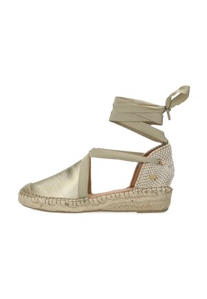 Espadrille de cuero dorado con tiras de tela beige, suela de yute trenzado y textura tejida en el talón. Diseño elegante y abierto.