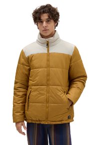 Chaquetón acolchado en amarillo mostaza con una sección superior en gris claro. Cuenta con un cuello alto, cremallera frontal y bolsillos laterales. Tejido texturizado.