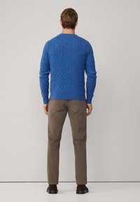 Jersey de punto azul con patrón de trenzas, cuello redondo y puños de canalé, combinado con pantalones marrón claros y zapatos oscuros.