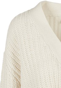 Chunky vit stickad tröja med djup V-ringning och ribbade detaljer. Texturerad tyg med lös väv. Idealisk för lager-på-lager-styling.