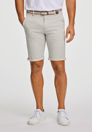 Beige, checkered shorts with rolled cuffs, equipped with pockets. Accompanied by a braided belt and white sneakers.