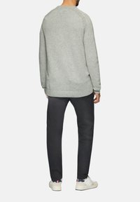 Jasnoszary sweter dzianinowy z okrągłym dekoltem, prążkowanym wykończeniem i fakturowanym materiałem. Połączony z ciemnymi spodniami i casualowymi białymi sneakersami.