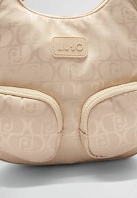 Borse Liu Jo in beige chiaro, caratterizzata da un tessuto testurizzato con un sottile motivo a logo. Include due tasche frontali e un'etichetta con il marchio.
