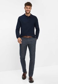 Polo a maniche lunghe blu navy, abbinato a pantaloni grigio scuro con trama e cintura marrone, completato da mocassini marroni. Design semplice, vestibilità casual.