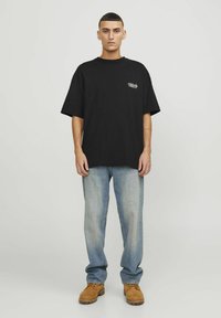 T-shirt in cotone nero con maniche corte e scollatura rotonda, con un piccolo logo bianco. Abbinato a jeans azzurri e stivali marroni.