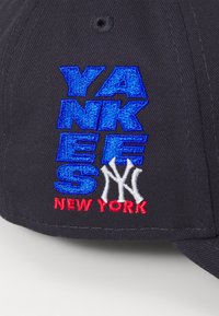 Cască sport gri închis cu broderie albastră "YANKEES", logoul alb "NY" și "NEW YORK" roșu. Fabricată din țesătură, cu o formă structurată.