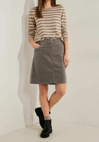 Beige ja ruskea raidallinen neule yhdistettynä harmaaseen corduroy-polvimittaiseen hameeseen, jossa on kaksi etutaskua ja kaksi nappia vyötäröllä.
