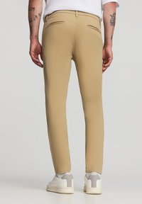 Khaki chinos o slim fit, z dwiema tylnymi kieszeniami i gładką fakturą; zestawione z białymi sneakerami i jasnoskalnymi skarpetkami.