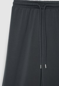 Dunkelgraue Jogginghose aus weichem Stoff mit elastischem Bund, verstellbarem Kordelzug und minimalistischem Design.