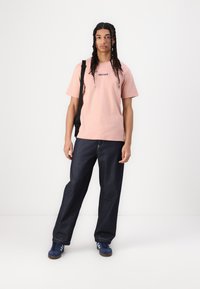 Lyserød bomulds T-shirt med "element" trykt i blå, parret med mørkeblå, løs siddende denim jeans og blå sneakers.
