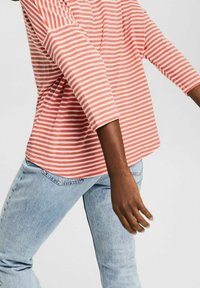 Červeno-bílý pruhovaný dlouhý rukáv, vyrobený z měkké bavlny, s volným střihem. Kombinováno se světle modrými džíny.