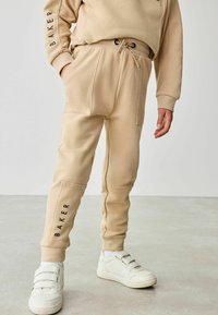 Khaki joggerbukser med elastisk liv og snøre, med sidelommer, subtil tekst "BAKER" på venstre ben og glat stofstruktur.