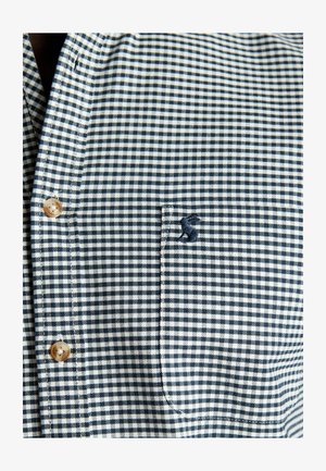 Tumesinise ja valge ruudulise mustriga nööbitav särk, millel on väike tikitud detail taskul. Klassikaline krae ja puidust nupud.