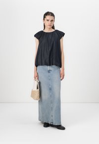 Mørkeblå kortermet topp med en sammensydd hals, kombinert med en lys blå denim maxiskjørt, holder en teksturert beige håndveske.