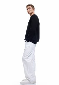Sudadera negra de manga larga, cuello redondo y puños acanalados, combinada con pantalones blancos de corte holgado y zapatillas blancas.