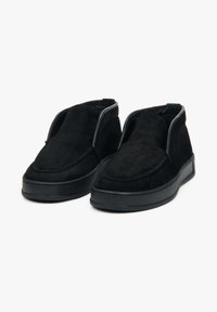 Czarne zamszowe buty wsuwane z okrągłym noskiem, niską gumową podeszwą i minimalnym przeszyciem. Posiadają miękką teksturę i elegancki kształt.