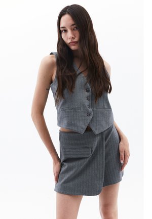 Gilet gris sans manches avec cinq boutons et deux poches avant, associé à un short taille haute assorti avec une poche latérale.