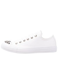 White canvas sneaker featuring a round toe with metallic spikes, lace-up design, and rubber sole with textured toe cap.