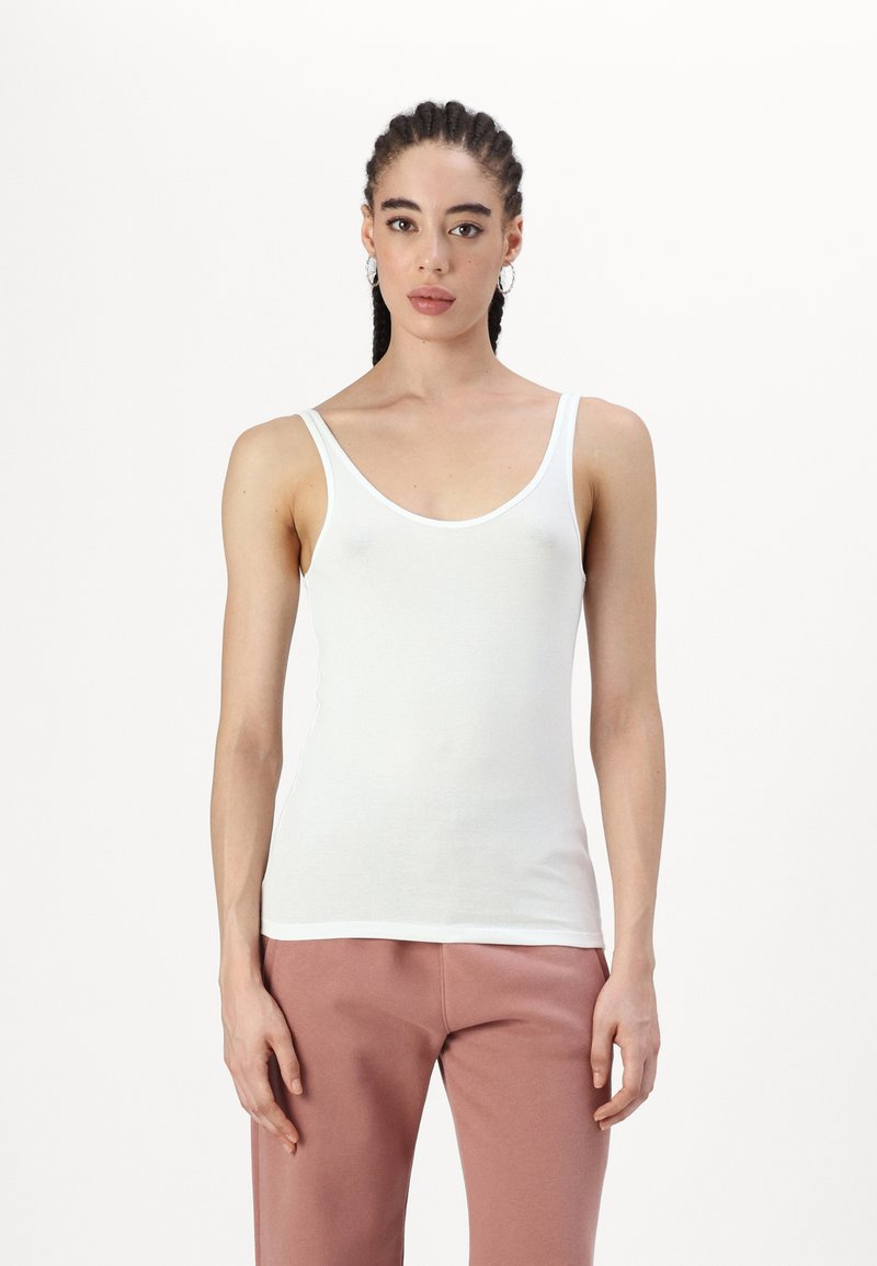 Top blanco sin mangas con tirantes anchos, material de algodón suave, diseño ajustado y escote redondeado, combinado con pantalones de chándal rosas.