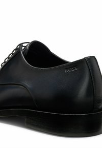 Scarpa in pelle nera con superficie liscia, cuciture sottili e punta rotonda. Presenta un piccolo logo sul tallone e una suola elegante e resistente.
