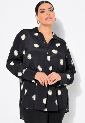Schwarze Bluse mit großen weißen Pinselstrichflecken, Knopfverschluss, Kragen, langen Ärmeln und Seitenschlitzen für zusätzlichen Komfort.