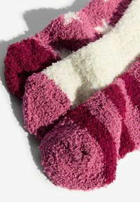 Pihe-puha, csíkos zoknik pink és burgundi árnyalatokban, lágy, textúrált felülettel. A felgöngyölt szélek kiemelik a színátmeneteket.