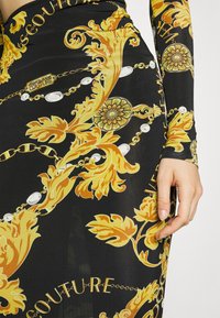 Melna kleita ar zelta baroka rakstu, ar ķēdēm, ziedu akcentiem un zīmola logotipiem. Garām piedurknēm ar teksturētu audumu.