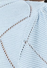 Lichtblauwe gebreide stof met een reliëfpatroon en open geweven delen, die een diagonaal lijn ontwerp creëren.