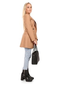 Tan blazer met een getailleerde pasvorm, gecombineerd met lichtblauwe skinny jeans. Zwarte enkellaarsjes en een gestructureerde zwarte handtas maken de look af.