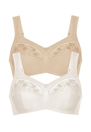 Woman standing barefoot wearing matching white lingerie with floral lace details on bra cups and panties against a plain background.