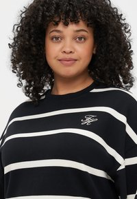 Sort og hvid stribet sweatshirt med rund halsudskæring, løs pasform og broderet "FH" logo på brystet. Blød stoftekstur.